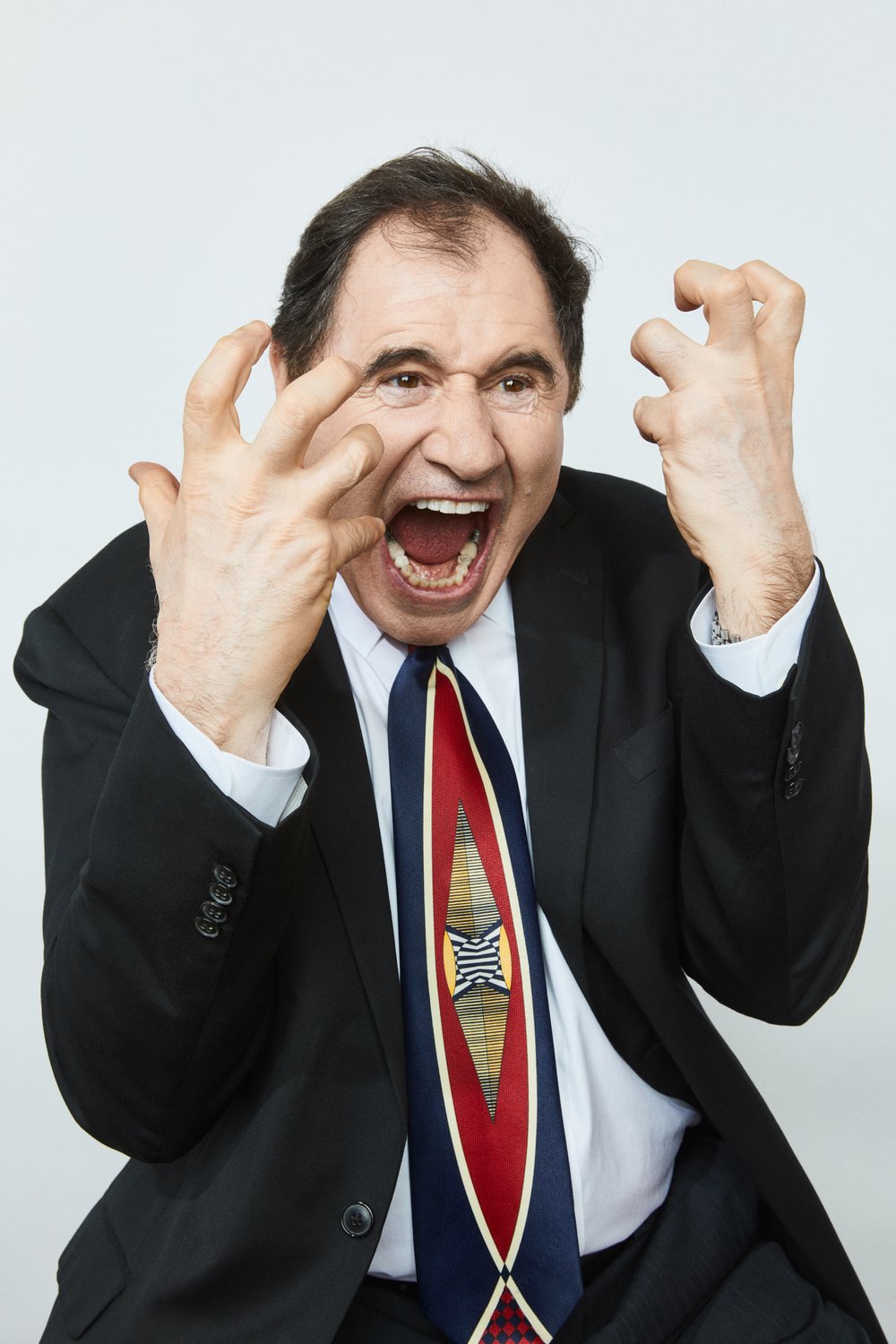 A man in a suit and tie yells with his hands up in an indoor setting, expressive and intense, capturing a moment of strong emotion.