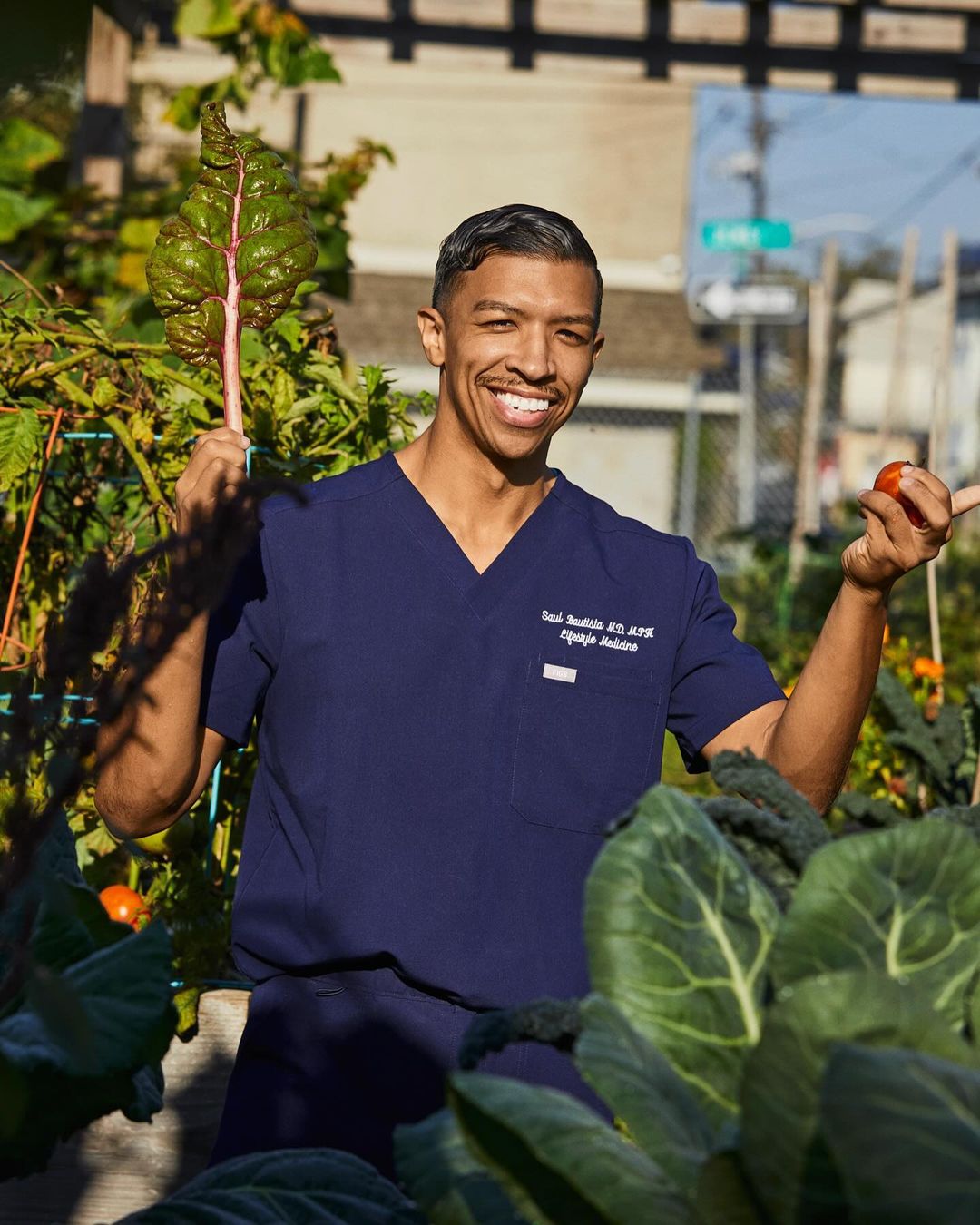 Smiling man in scrubs in a garden, holding fresh produce in sunlight. Focus on health, nutrition, and wellness in an outdoor setting.