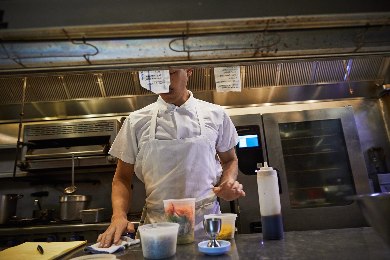 Chef in a commercial kitchen preparing food with various containers and kitchen equipment. The environment is stainless steel.