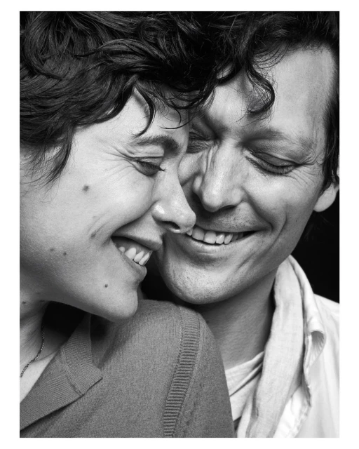 Black and white portrait of a smiling couple, a woman and a man, embracing closely with dark curly hair in an indoor setting.
