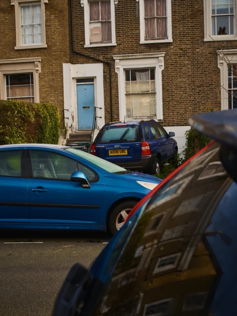 Blue car parked on an urban street in front of a brick building with white trim, windows, and a blue door, capturing a residential scene.
