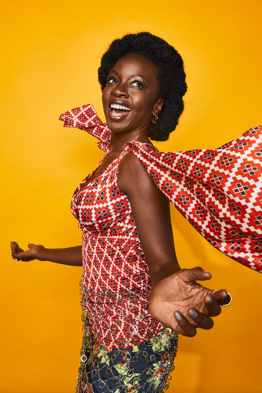 Portrait of an adult woman with a joyful expression wearing a patterned dress with an orange background in a photo studio setting.