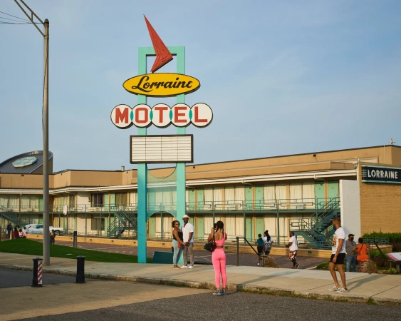 Exterior of the Lorraine Motel with vintage sign and people walking in front on the street during daylight under clear blue skies.