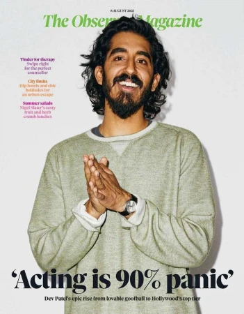 Magazine cover featuring Dev Patel, with dark hair and beard, wearing a casual sweater, hands together, in front of a white background.