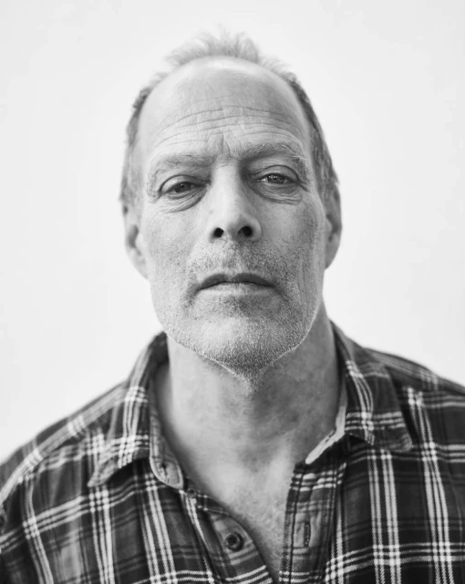 Black and white portrait of an adult man in a plaid shirt against a plain background, captured in a close-up shot with soft lighting.