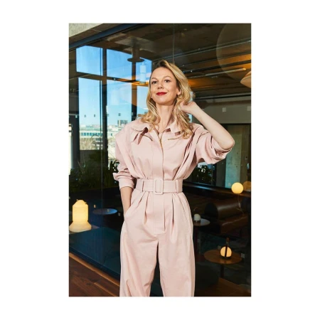 Portrait of a blonde woman wearing a pink belted jumpsuit standing in a modern office interior