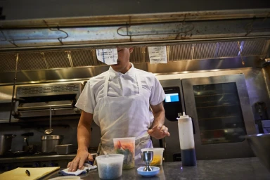 Chef in white apron wiping down stainless steel restaurant kitchen counter