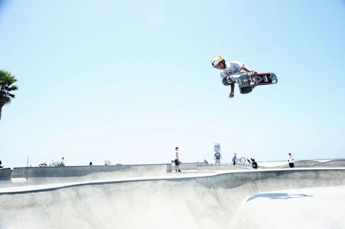 Skater mid-air performing a trick above a concrete skatepark bowl under a clear sky