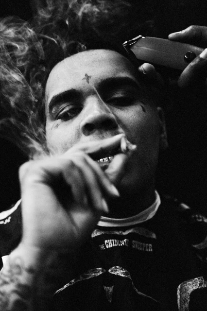 Black and white portrait of a man with a tattoo smoking, getting a haircut from an electric razor, with smoke around his head.