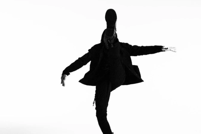 Monochrome portrait of a person in black clothing kicking high against a plain white background