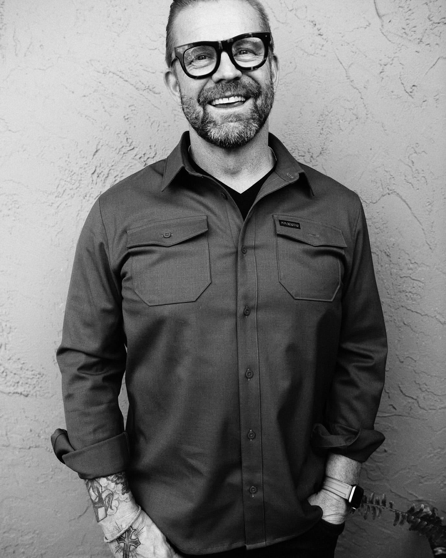 Portrait of a smiling man in thick-rimmed glasses and a button-down shirt photographed by Jeff Forney.