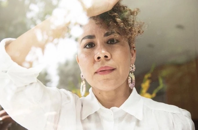 Portrait of a woman with curly hair wearing a white shirt and decorative earrings, photographed by Jeff Forney.