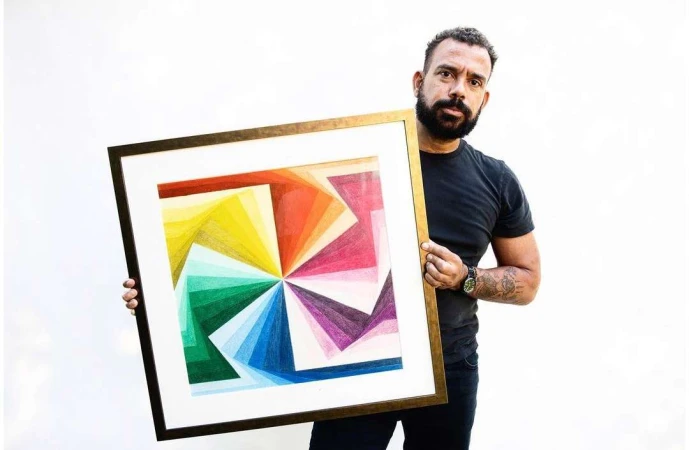 Man holding a framed square geometric color gradient artwork against a plain white wall