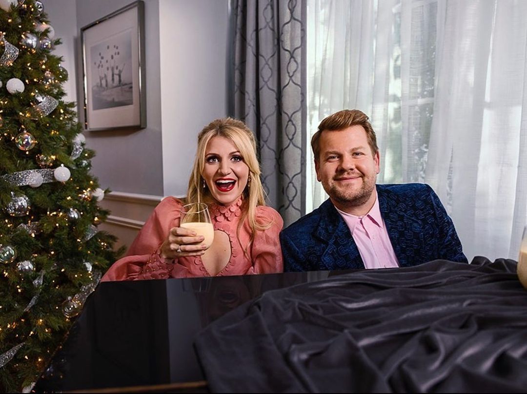 Festive indoor scene featuring a woman holding a glass of eggnog and a man in a blue jacket near a decorated Christmas tree.