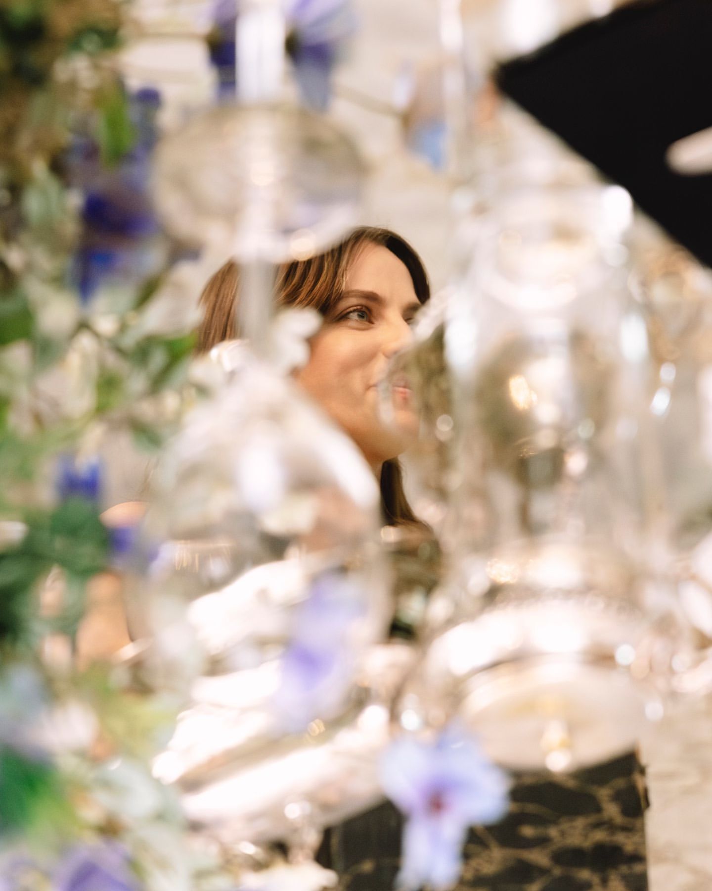 Woman viewed through heavily blurred foreground glassware and floral arrangements in Los Angeles