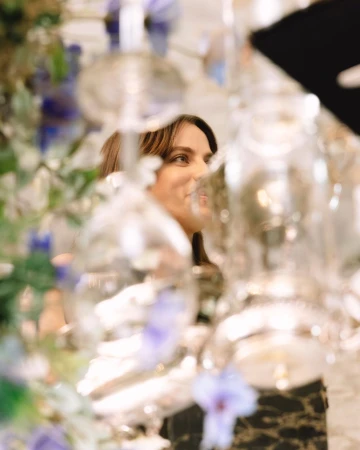 Woman viewed through heavily blurred foreground glassware and floral arrangements in Los Angeles