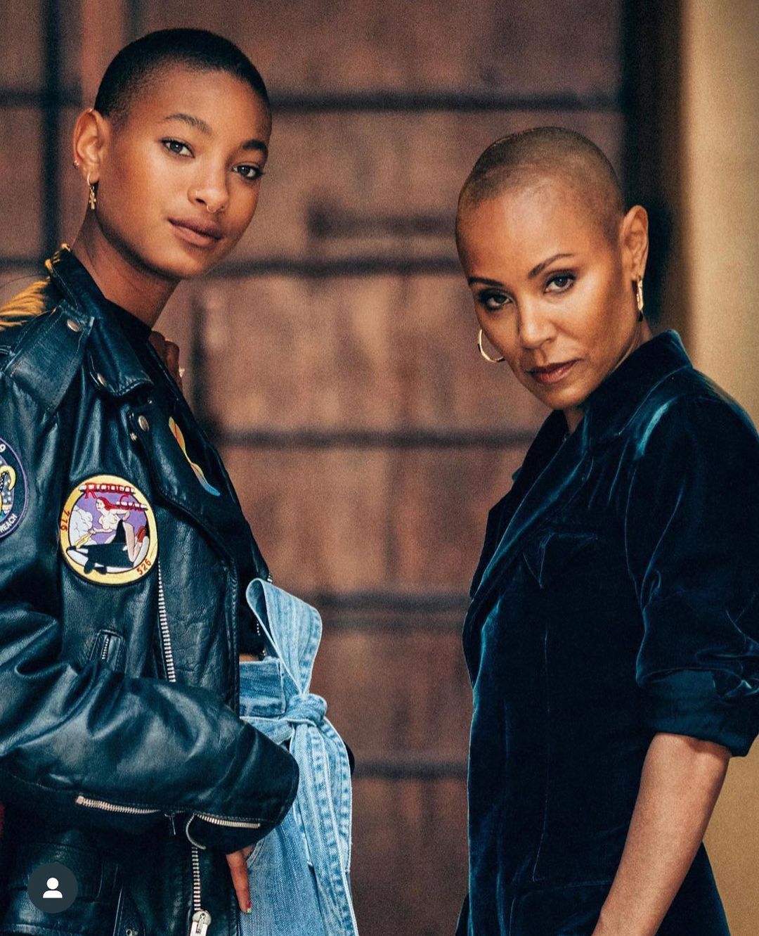 Two women with short hair posing indoors. One wears a leather jacket and the other a velvet blazer in a portrait-style photograph.
