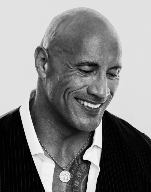Close-up portrait of a smiling, bald adult male wearing a vest and collared shirt against a white background in black and white.