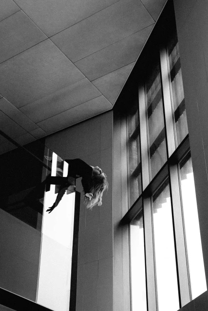 Abstract black and white architectural shot with woman in a dark dress reflected in glass near large windows. Monochrome photography.