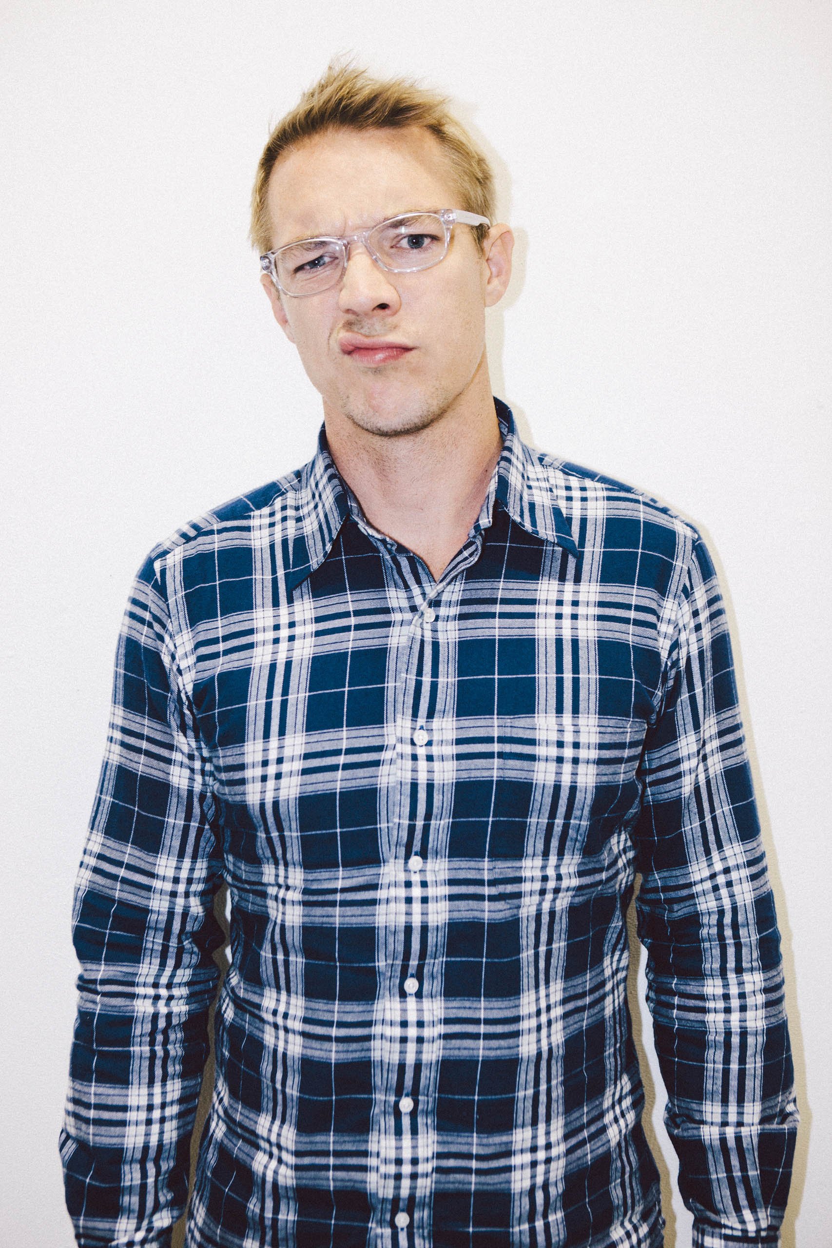 Man wearing blue and white plaid shirt and clear-frame glasses against a plain white background
