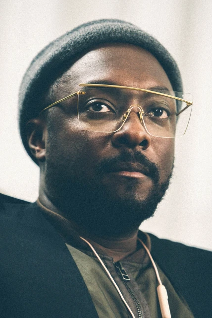 Close-up studio portrait of an adult male wearing glasses, a black beanie, and a black jacket, captured in a well-lit indoor setting.