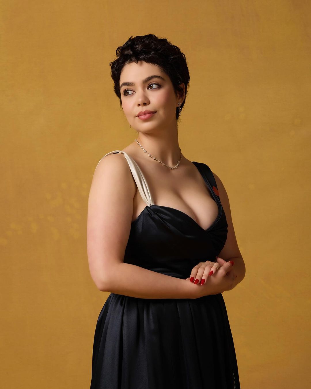 Portrait of a woman with dark hair and a black dress against a warm yellow background, looking off to the side with a slight smile.