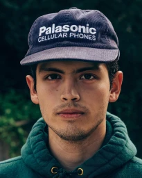 Portrait of a young man wearing a dark corduroy baseball cap and a green hoodie, photographed by Huy Doan.