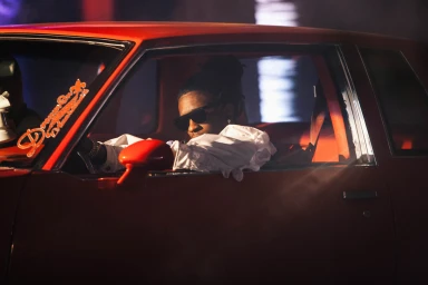 Man wearing sunglasses and a white shirt sitting inside a red car at night