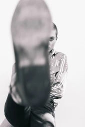 Close-up portrait of a person with a shaved head wearing a star-patterned button-down shirt, with a boot blurred in the extreme foreground.