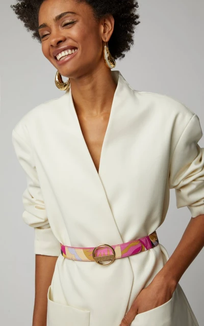 Elegant Black woman in cream-colored jacket dress with geometric-patterned belt, smiling slightly with gold hoop earrings. Beauty shot.