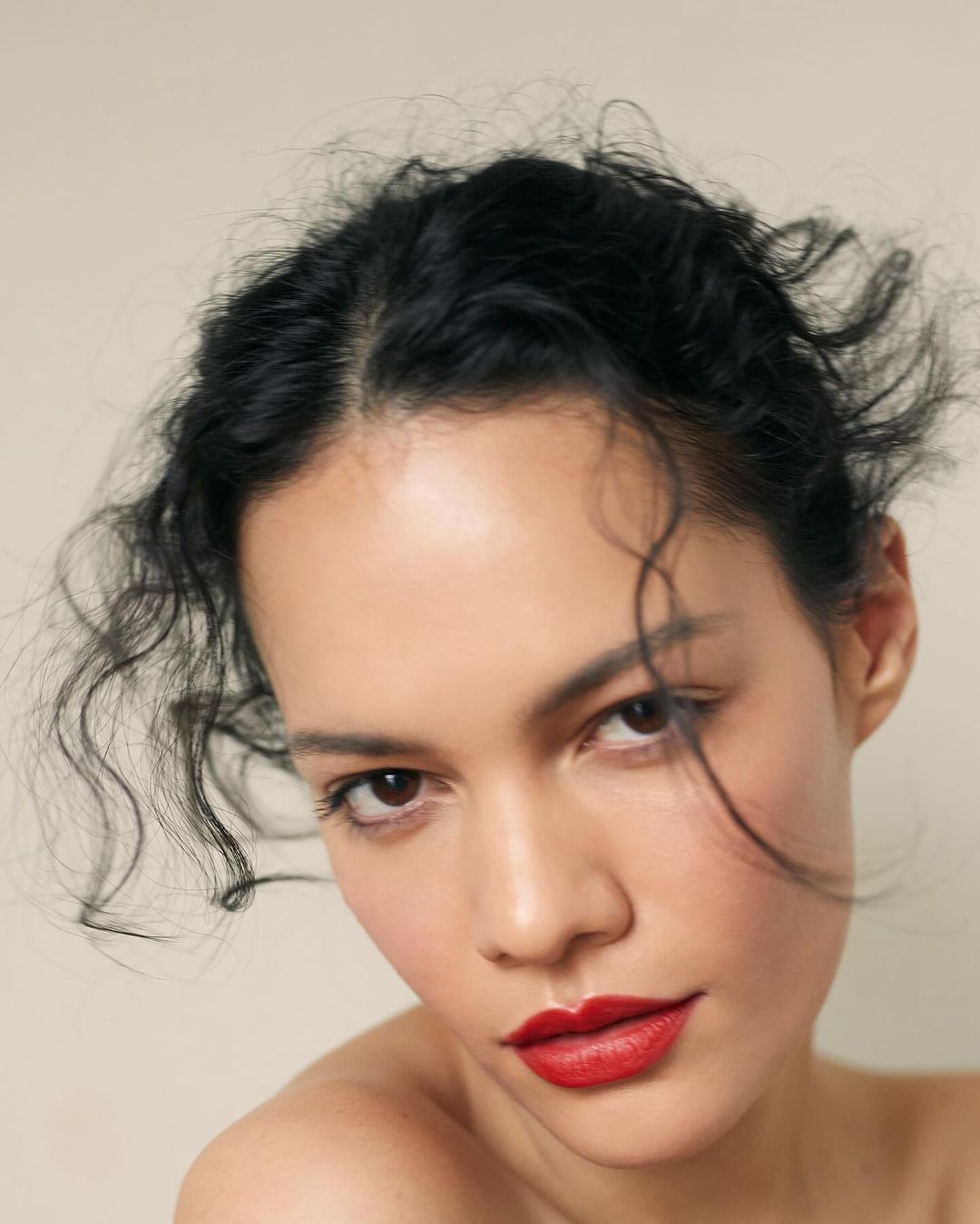 Close-up portrait of a woman with dark hair and vivid red lipstick against a plain light background