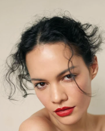 Close-up portrait of a woman with dark hair and vivid red lipstick against a plain light background