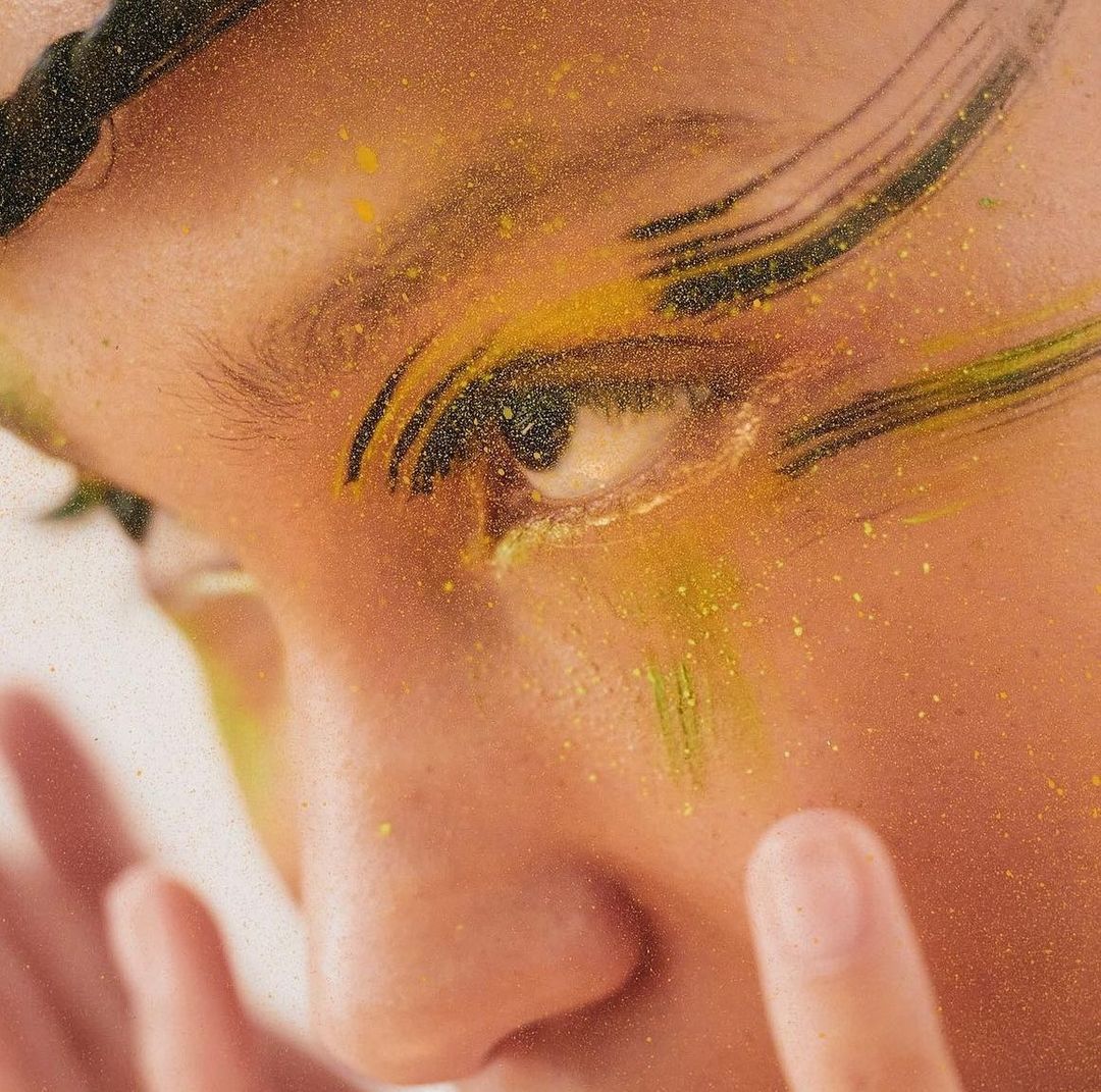Close-up of a person with yellow and black paint on their face, focusing on the eye and skin texture, artistic makeup, and creative design.