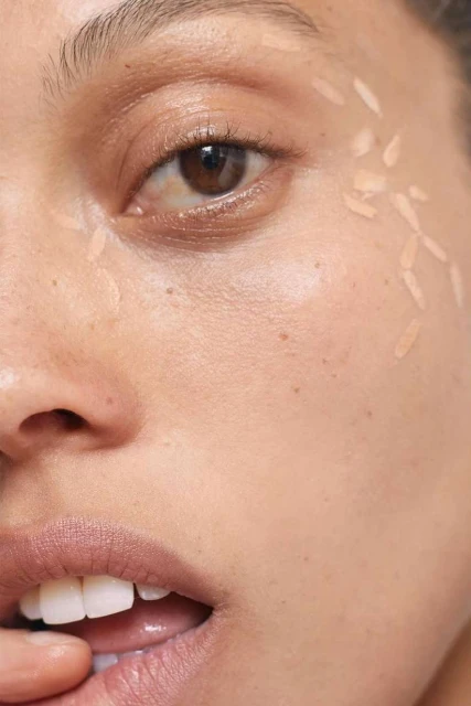 Close-up of a woman's face with makeup dots accentuating her eye and cheek, showcasing beauty and cosmetic application.