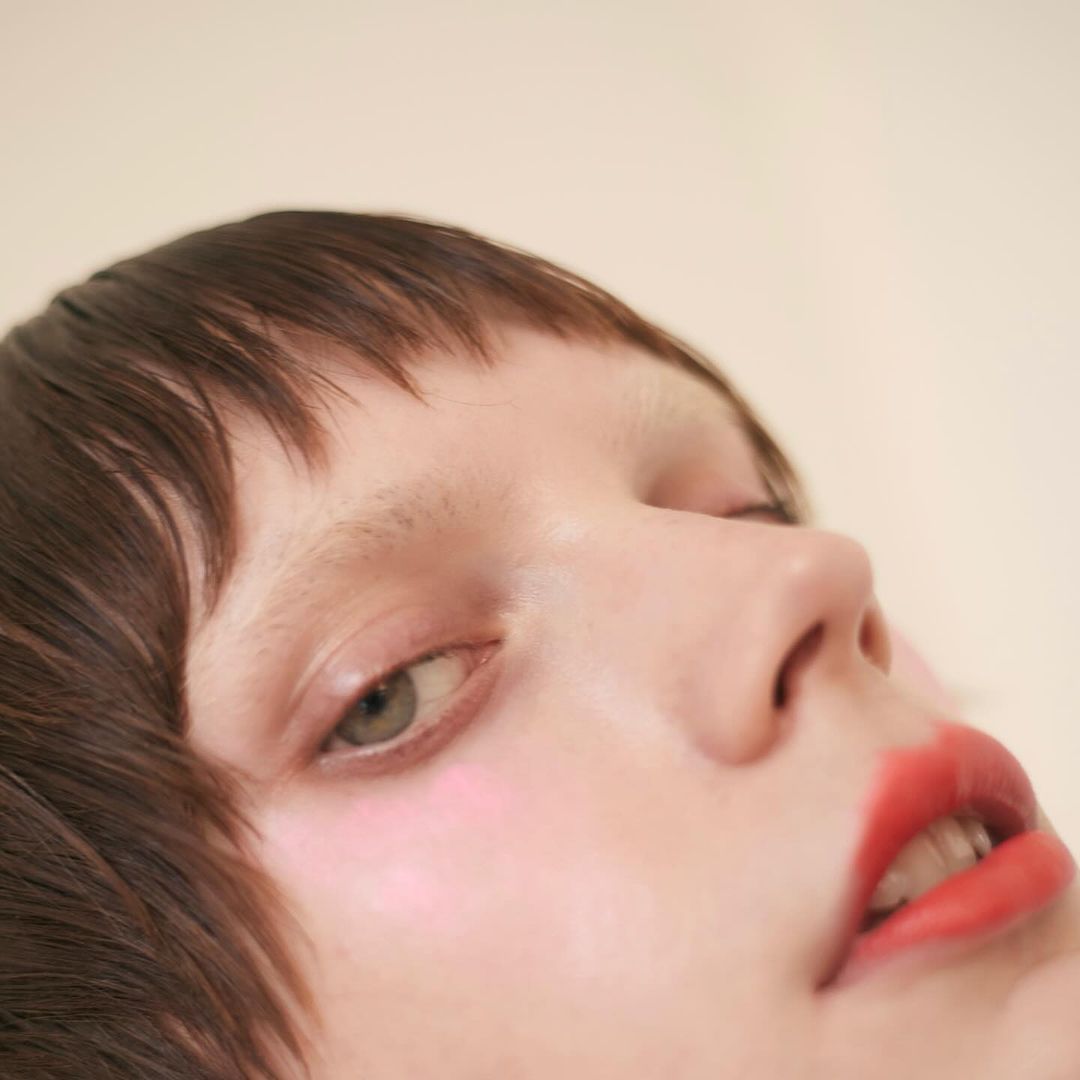 Close-up portrait of a woman with dark hair and bright red lips against a neutral background