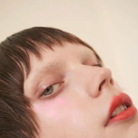 Close-up portrait of a woman with dark hair and bright red lips against a neutral background