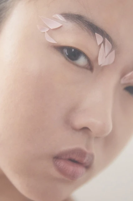 Close-up portrait of an Asian woman with petal eyebrow art in a soft, diffused light. Beauty and creative makeup concept.