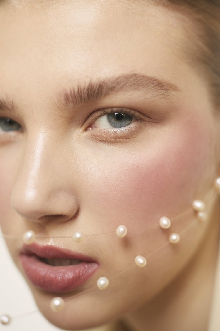 Close-up beauty portrait of a woman wearing a delicate pearl necklace strand draped across her face by photographer Viviane Black.