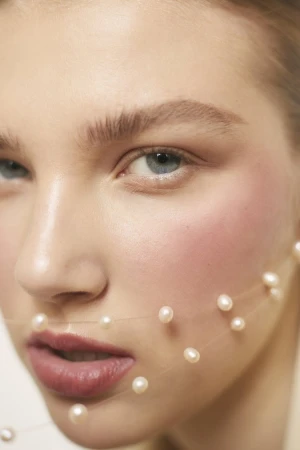 Close-up beauty portrait of a woman wearing a delicate pearl necklace strand draped across her face by photographer Viviane Black.