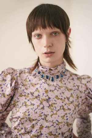 Portrait of a model with short fringed hair wearing a pink floral blouse and blue jewel necklace