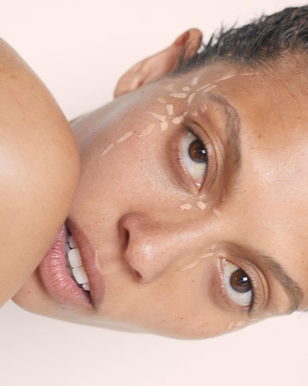 Close-up portrait of a woman with tan skin and brown eyes, wearing makeup, posing in front of a neutral background in a beauty shot.