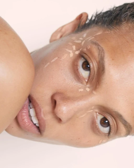 Close-up portrait of a woman with tan skin and brown eyes, wearing makeup, posing in front of a neutral background in a beauty shot.
