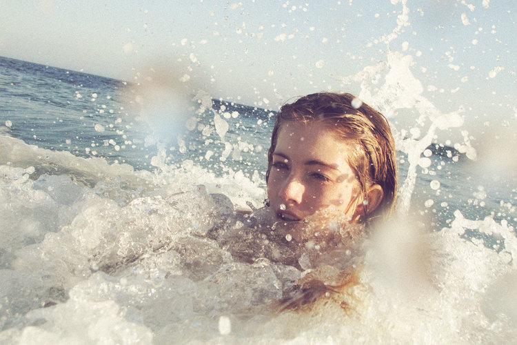 Woman in the ocean surrounded by splashing water, with pale complexion and light brown hair, captured with a shallow depth of field.