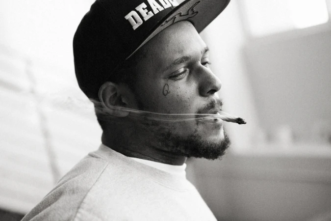 Black and white portrait of a man wearing a baseball cap smoking a cigarette by Bryan Sheffield