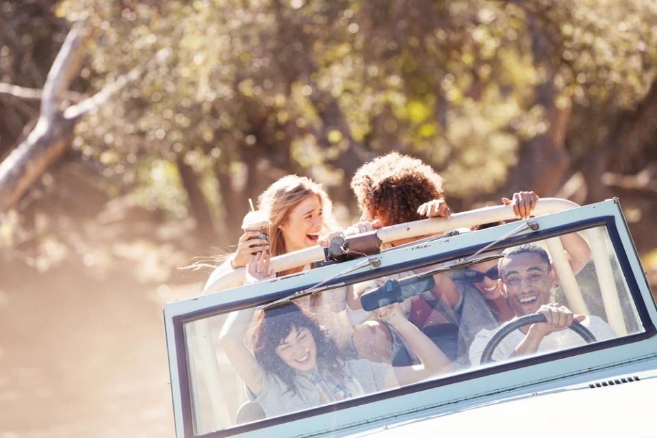 Four people ride in a jeep on a sunny day. The open-air vehicle moves along a tree-lined path with happy passengers. 