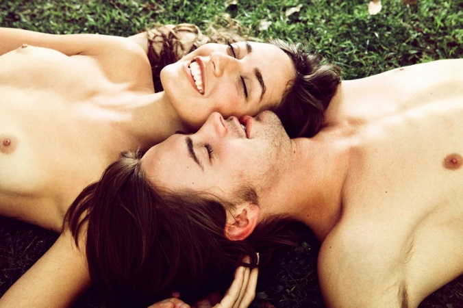 Close-up portrait of a smiling woman and a man lying together on green grass under natural light.
