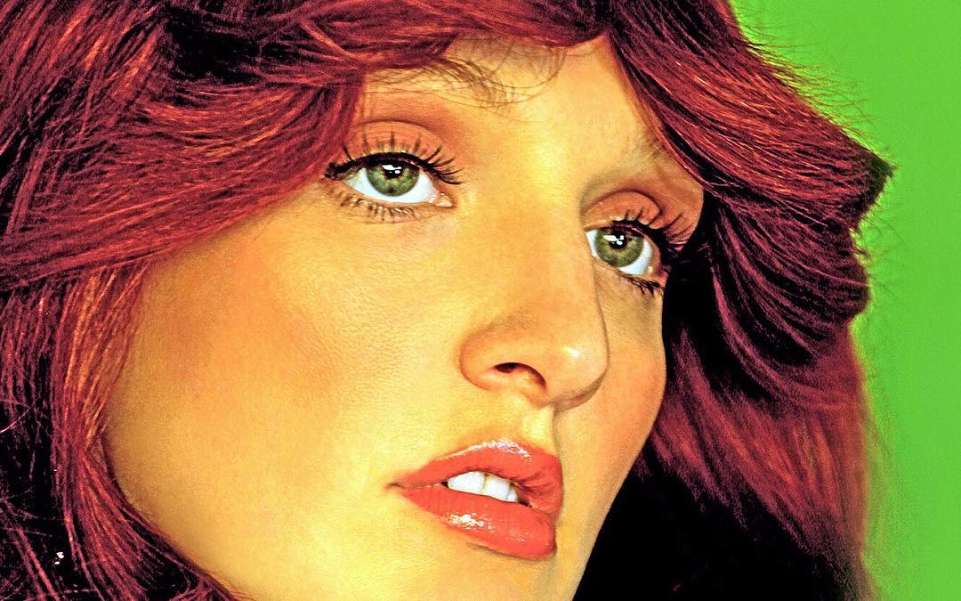 Close-up portrait of a person with red hair and green eyes against a bright green background, showcasing makeup and hairstyle.
