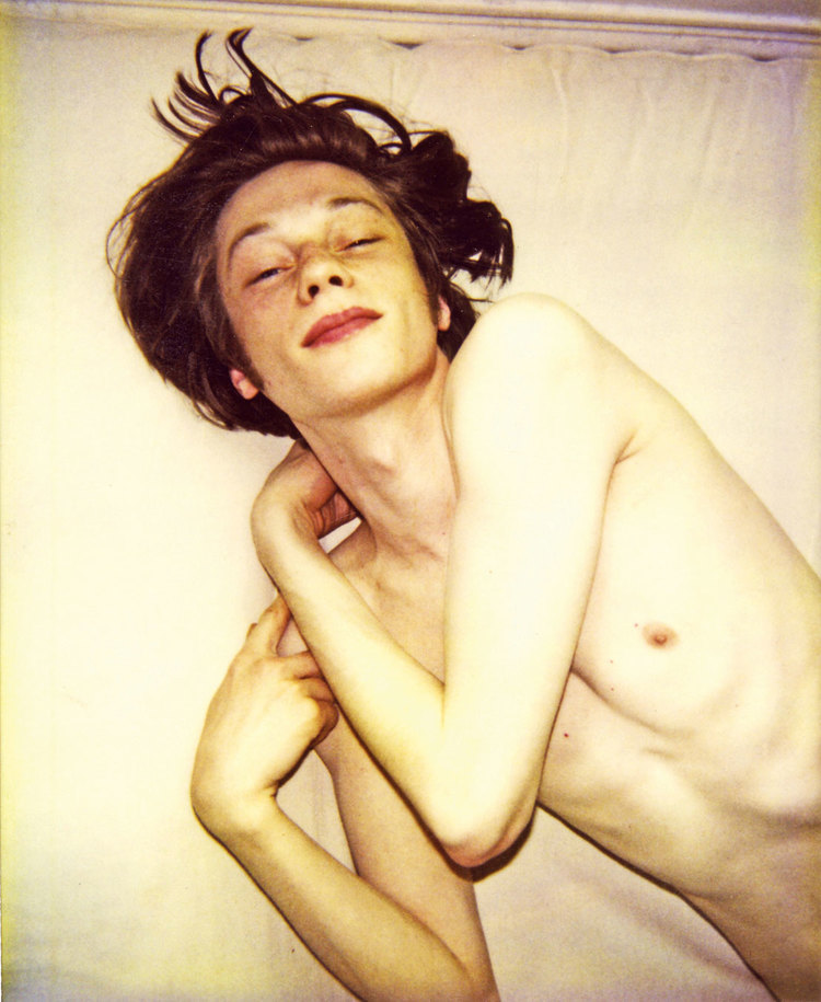 Artistic portrait of a bare-chested fair-skinned young adult lying on a white surface with a serene expression and eyes closed.