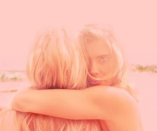 Close-up portrait of two blond women embracing tightly under a warm monochromatic pink filter.