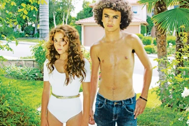 Young woman in white bodysuit and young man with curly hair posing outdoors on a suburban street by photographer Stephanie Vovas